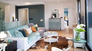 Ein modernes Wohnzimmer mit einer Couch, einem Glastisch, einem Kuhfellteppich und Meerblick durch ein großes Fenster.