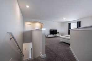 Uma sala de estar moderna com uma TV de tela plana, um sofá branco e piso coberto de carpete.