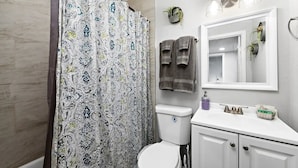 Un bagno con una tenda da doccia fantasia, un water, un lavandino con specchio e asciugamani appesi al muro.