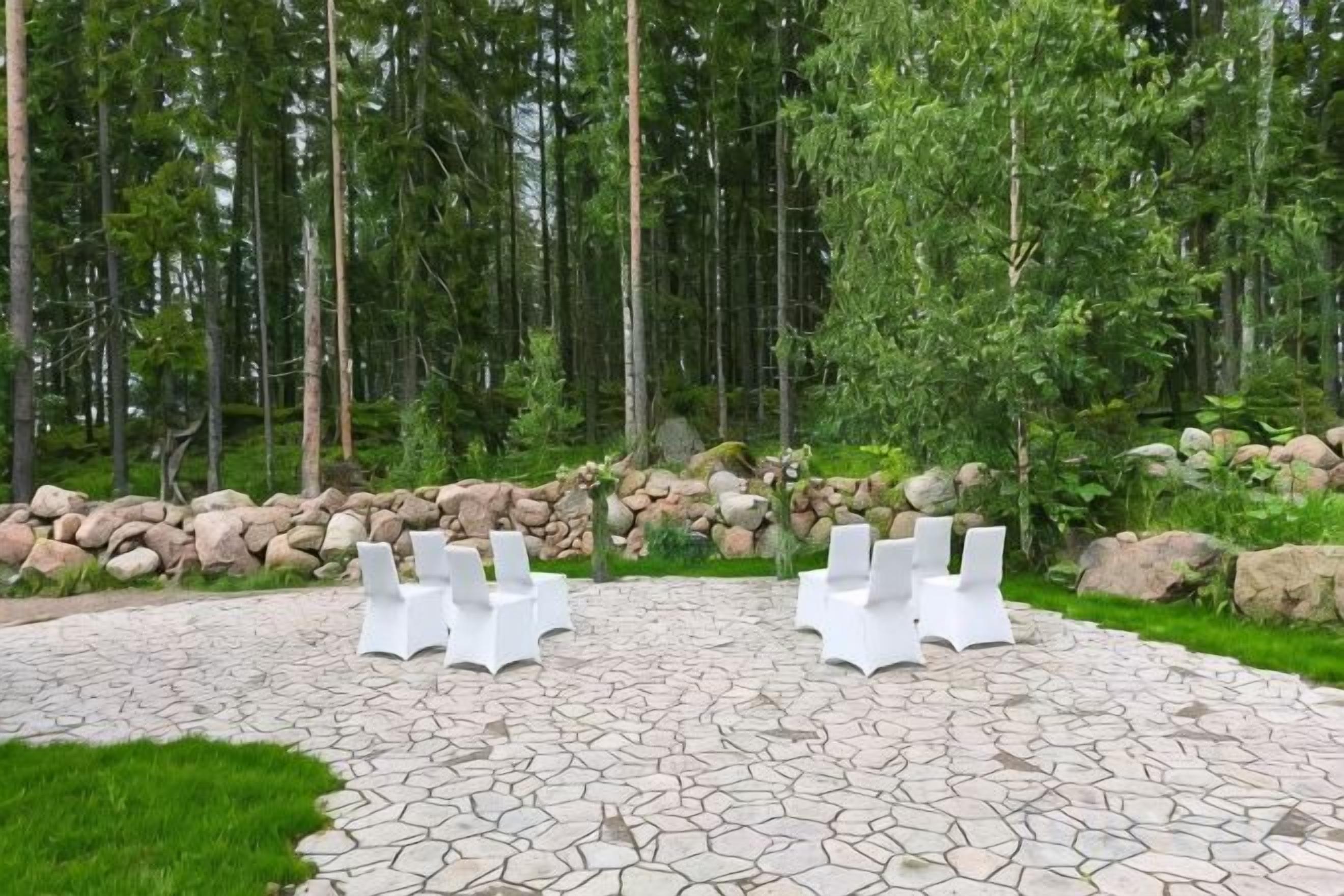 Ulkoalue, jossa on valkoisia tuoleja kivilaatoitetulla pinnalla, ja aluetta ympäröi luonnonmukainen metsämaisema.