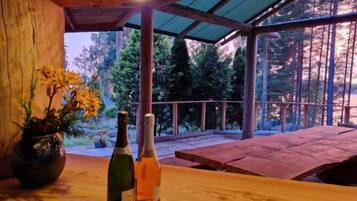 Une table en bois, avec deux bouteilles, une plante en pot et une vue sur une forêt, visible à travers une paroi vitrée.