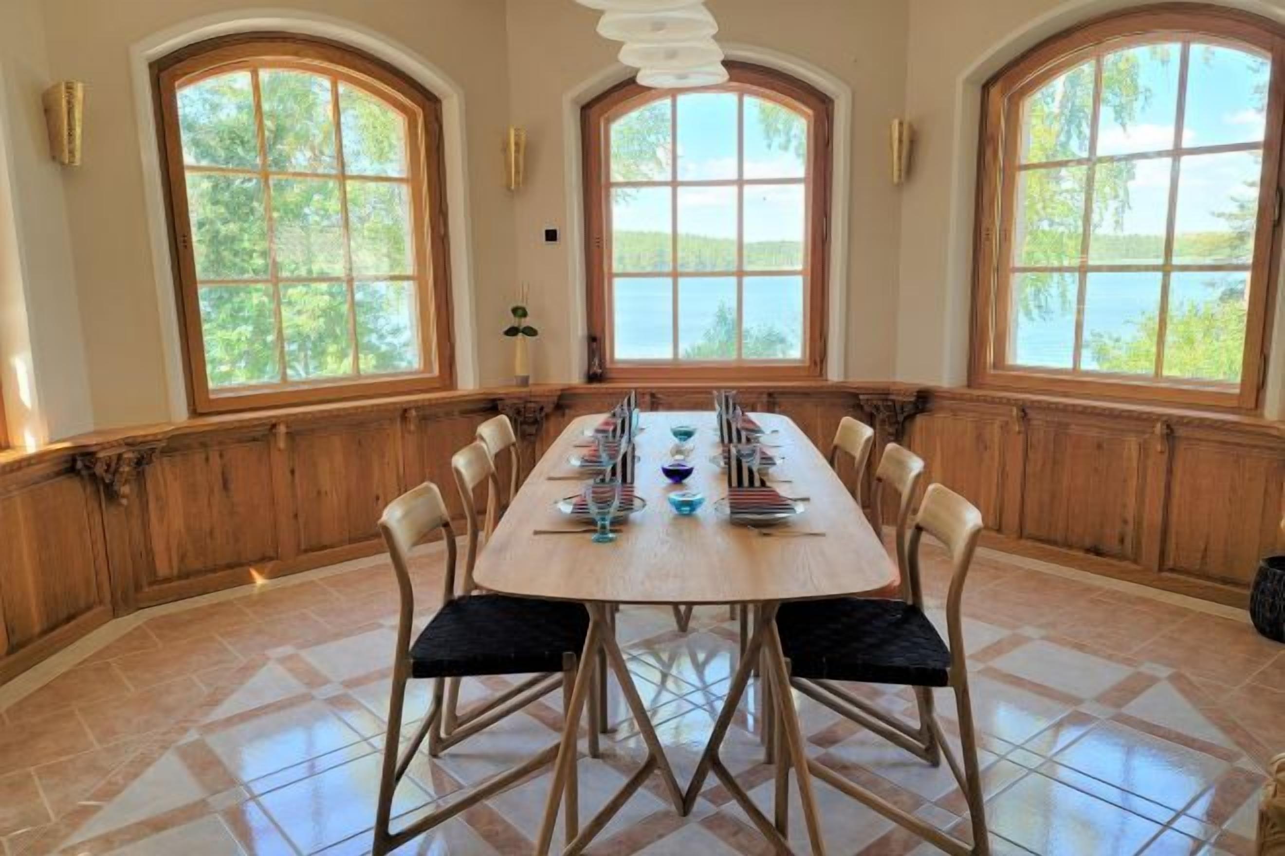 Un espace repas avec une longue table, des chaises et de grandes fenêtres.