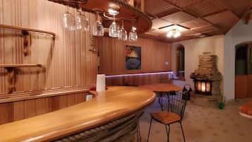 Área de bar com balcão de madeira, luminárias pendentes e lareira de pedra.