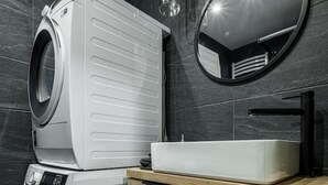 Une salle de bain moderne avec un lave-linge et un sèche-linge superposés, un meuble-lavabo en bois et un grand miroir.