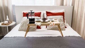 Un lit bien fait, avec un plateau de petit-déjeuner comprenant une cafetière, un muffin et une tasse à thé, dans une pièce dotée d’une grande fenêtre et de rideaux.