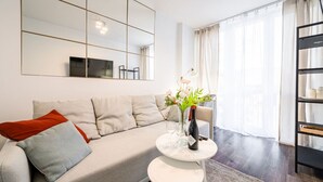 Un salon moderne avec un canapé, une petite table ronde ornée d’un vase de fleurs et une bibliothèque.