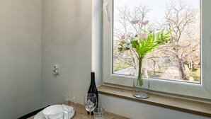 Un coin repas avec une table dressée pour deux personnes, une bouteille de vin et un vase rempli de fleurs placé près d’une fenêtre.