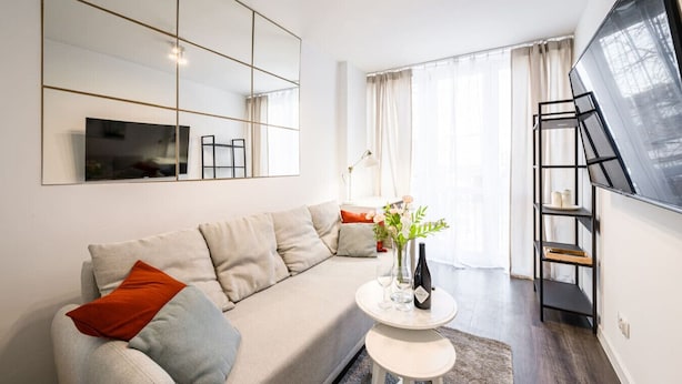 Un salon moderne avec un canapé, une table ronde ornée d’un vase et un grand miroir.