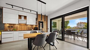 Een moderne keuken met witte kasten, een houten aanrecht en een eethoek met een grote tafel en stoelen.