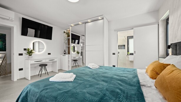 Een moderne slaapkamer met een bed, bureau, spiegel en kledingkast.