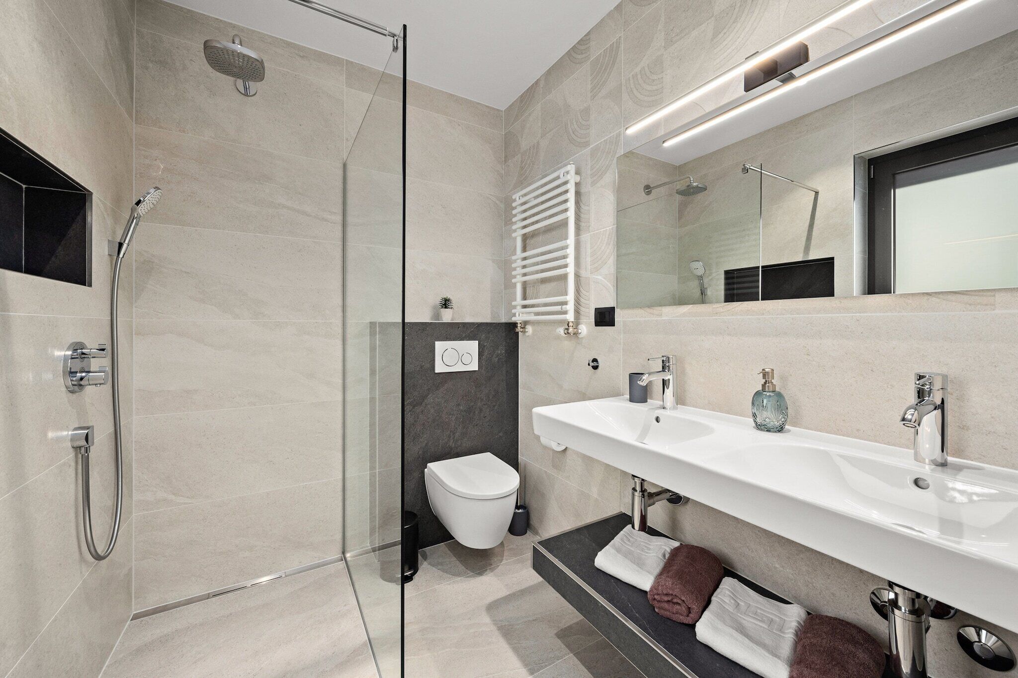 A modern bathroom with a glass-enclosed shower, a white sink, and a large mirror.