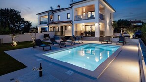 Een modern huis met twee verdiepingen, een zwembad, terrasmeubilair buiten en een goed verlicht terras.