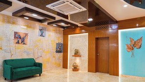 A lobby with a green sofa, artwork on the walls, a wooden door, and a ceiling with recessed lighting. - Sri Krishna Inn (Devanahalli)