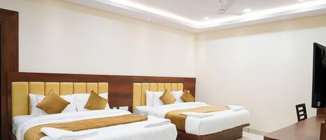 A hotel room with two beds, each with a wooden headboard and white bedding. There is a flat-screen TV on a wooden stand to the right.