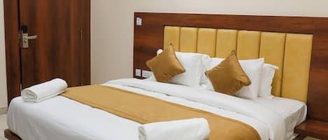 A neatly made bed with white and brown bedding, a wooden headboard, and a wooden door to the left.