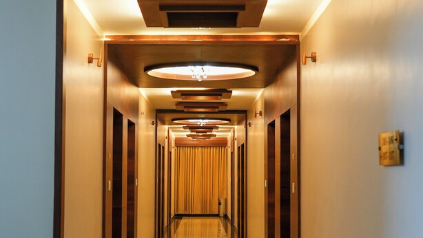 A long, well-lit corridor with a reflective floor, wooden paneling on the walls, and a ceiling with recessed lighting. - Sri Krishna Inn (Devanahalli)