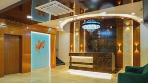 A hotel reception area with a modern design, featuring a reception desk, a chandelier, and a wall-mounted ski logo. - Sri Krishna Inn (Devanahalli)