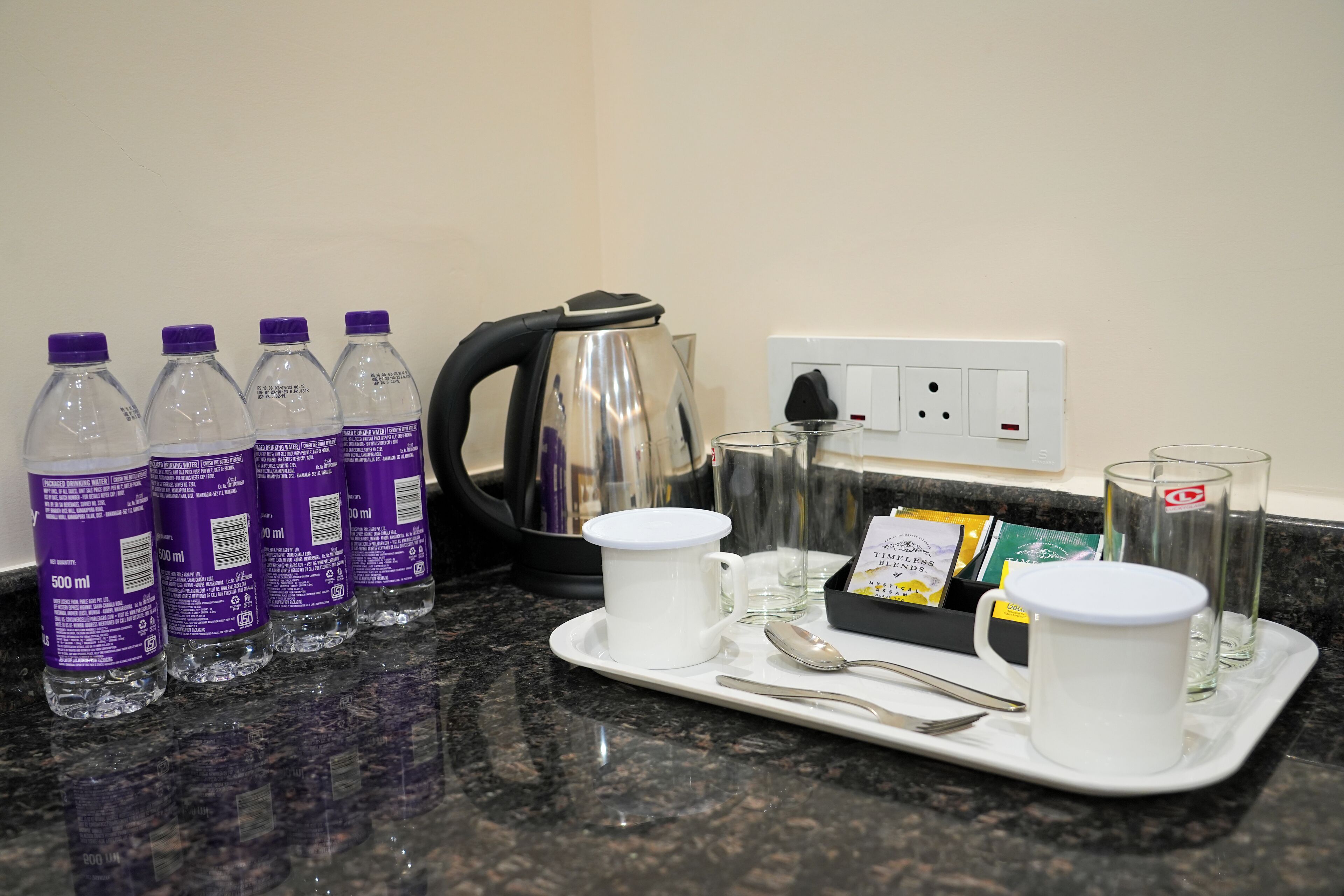 A tray with water bottles, a white mug, a tea box, and a spoon on a granite countertop.