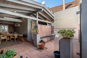 Un patio al aire libre con mesa y sillas, plantas en macetas y una parrilla.