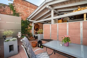 Un patio con una mesa, sillas, plantas en macetas y un muro de ladrillo.