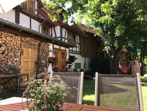 A traditional half-timbered building with a wooden door, a stone wall with stacked firewood, and a hanging chair.