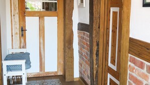 Une porte en bois avec un panneau de verre, un banc blanc orné de coussins à motifs et un mur de briques.