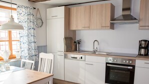 Une cuisine moderne avec des meubles blancs, un plan de travail en bois, un évier, un lave-vaisselle, un four et un luminaire suspendu.