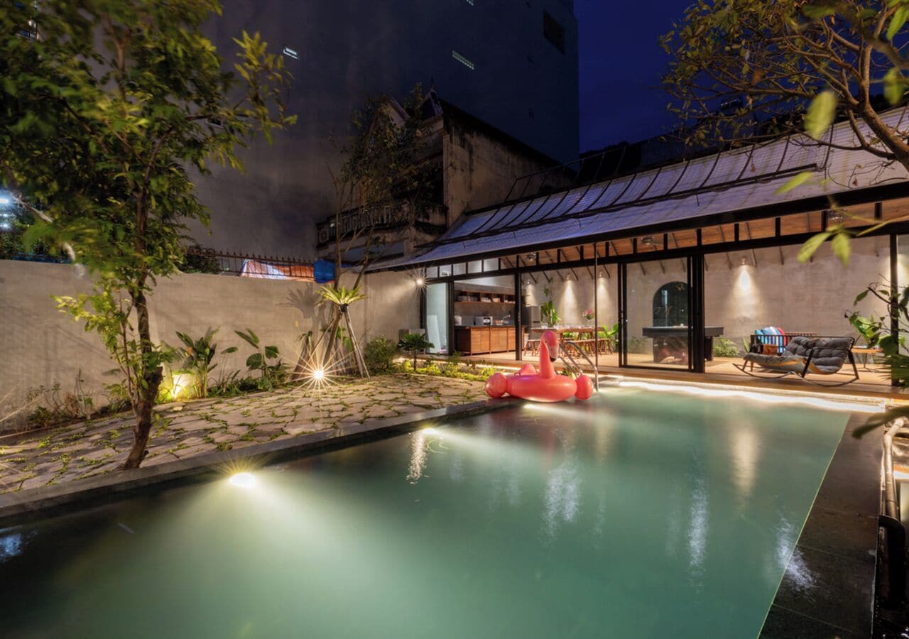 Una piscina con un juguete hinchable rojo, rodeada por una zona de patio con asientos y plantas.