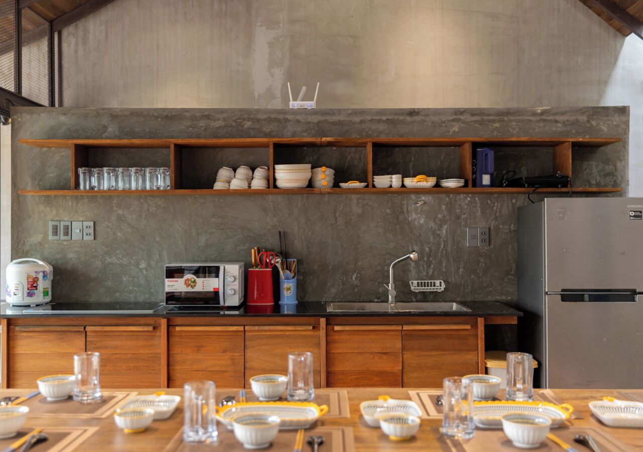 A modern kitchen with wooden cabinets, a built-in shelf with dishes, a refrigerator, and a dining area set for four.