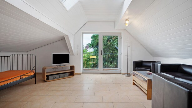 Une chambre de style loft moderne, dotée d’une lucarne, d’un lit, d’une télévision et d’un canapé.