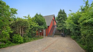 Un bâtiment rouge avec un escalier menant à une porte, le tout entouré de verdure.