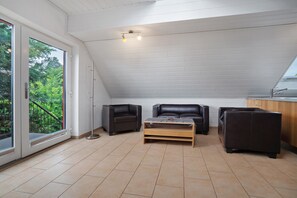 A modern interior with a sloped ceiling, a wooden coffee table, two black sofas, and a view through large glass doors.