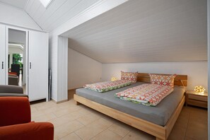 A bedroom with a loft-style ceiling, a bed with patterned bedding, a nightstand with a lamp, and a chair.