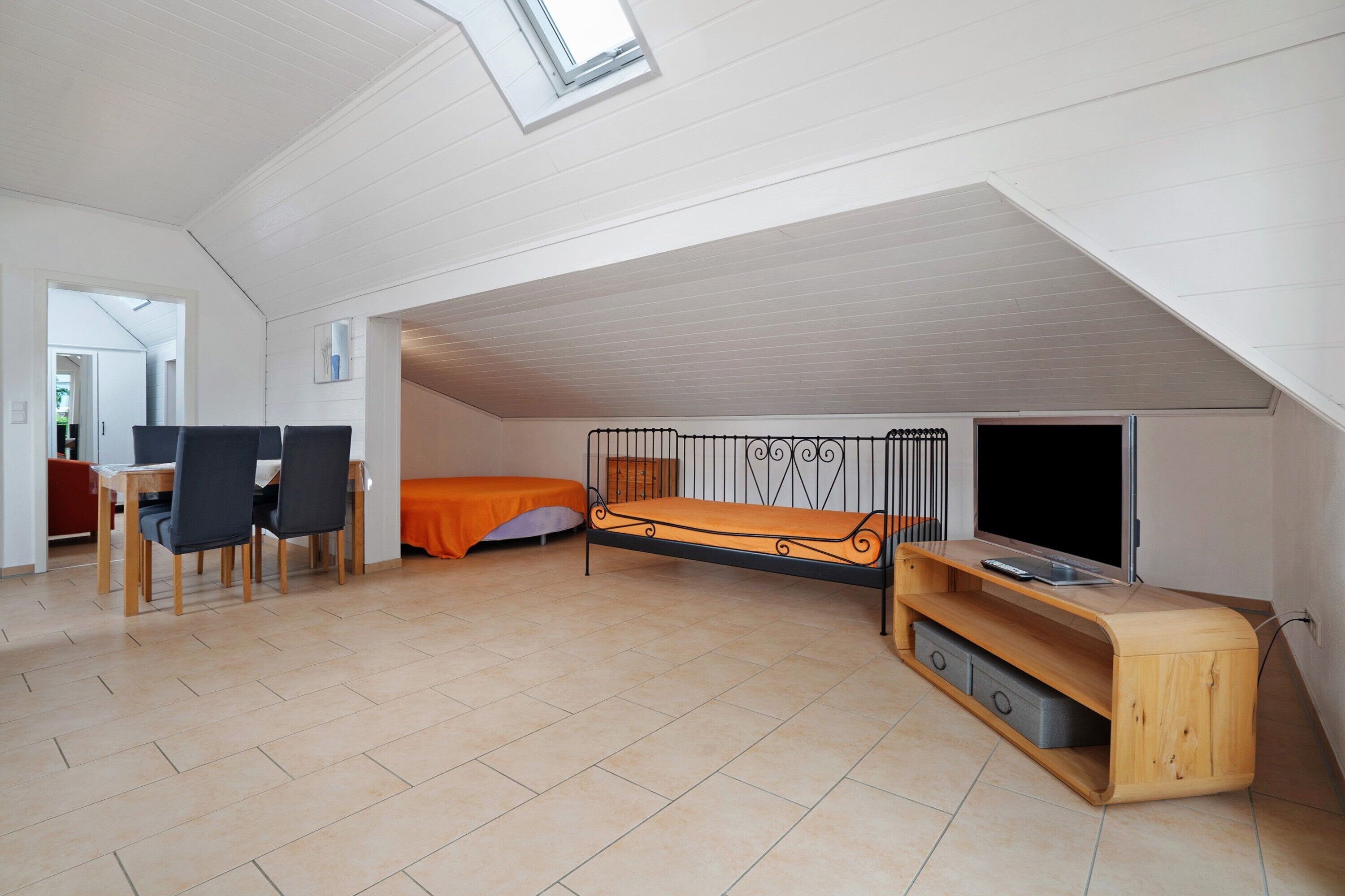 Une pièce de taille modeste comprenant un lit, un bureau, des chaises, un téléviseur et une lucarne.