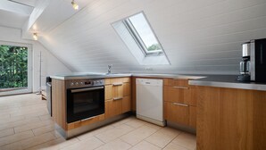 Une cuisine moderne dotée d’une verrière, d’un four encastré, d’un lave-vaisselle et de meubles de rangement en bois.