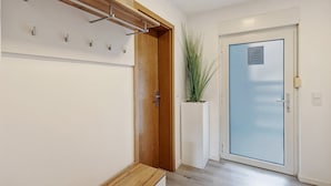 Un couloir avec un banc en bois, un porte-manteau, une plante en pot et une porte en verre dépoli.