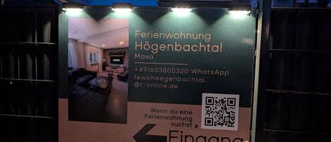 A sign for a hotel with a QR code, contact information, and an arrow pointing left.