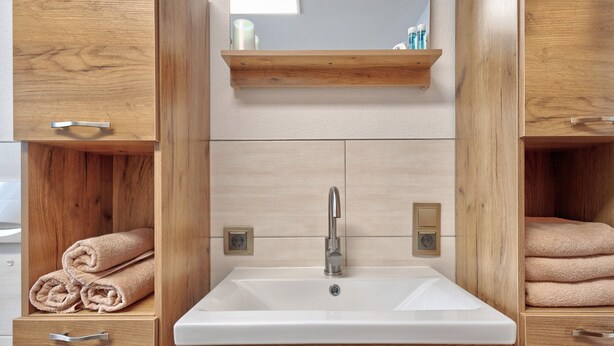 Une salle de bain avec un lavabo blanc, des meubles en bois et un miroir au-dessus du lavabo.