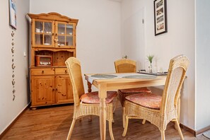 A dining area with a wooden table, wicker chairs with floral cushions, a wooden cabinet with glass doors, and a vintage radio. - Studio 'On the Island of Rügen' with Wi-Fi (Sagard)