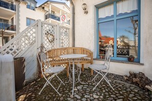 A patio with a round table and two chairs, a wooden bench, a white fence, and a building with a blue window. - Studio 'On the Island of Rügen' with Wi-Fi (Sagard)