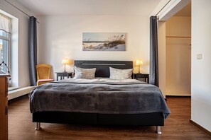 Une chambre à coucher avec un grand lit, deux lampes de chevet, une chaise, une fenêtre et un tableau au mur.