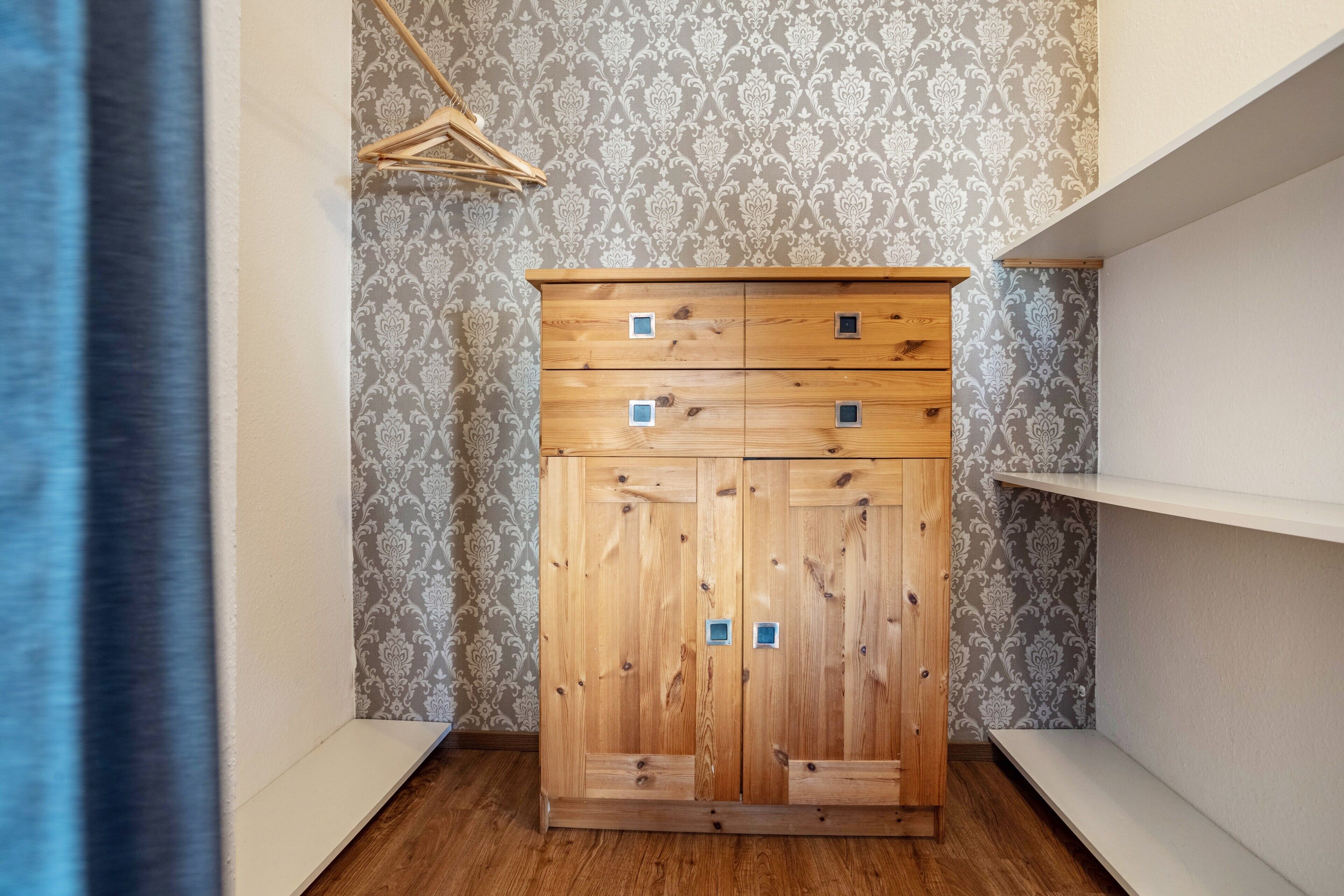 A wooden wardrobe with four drawers and two doors, set against a patterned wallpaper background.