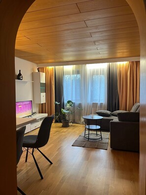 Una sala moderna con suelo de madera, un sofá, una mesa de comedor y un televisor.
