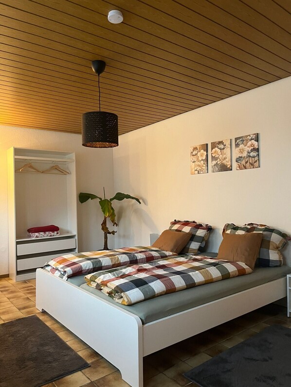 Un dormitorio con una cama, una lámpara colgante, una planta y decoración en la pared.
