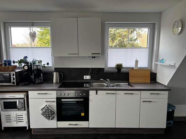 A modern kitchen with white cabinets, a built-in oven, a coffee maker, and a sink.