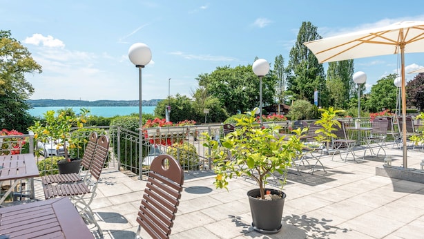 Eine Terrasse im Freien mit Tischen, Stühlen, Blumentöpfen und Blick auf das Wasser.