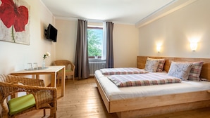 Ein Schlafzimmer mit zwei Betten, einem Tisch, Stühlen, einem Fernseher und einem Fenster mit Vorhängen.