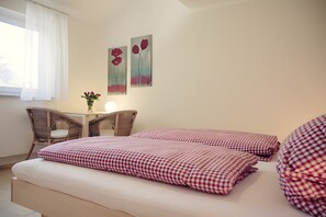Un dormitorio con una cama, dos almohadas a cuadros, una mesita de noche con un jarrón de flores y dos cuadros colgados en la pared.