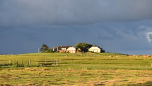 Un paysage rural avec des maisons sur une colline, un champ clôturé et un banc.