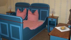 Une chambre avec un lit bleu, des oreillers à carreaux, une table de chevet avec une lampe et une commode en bois.